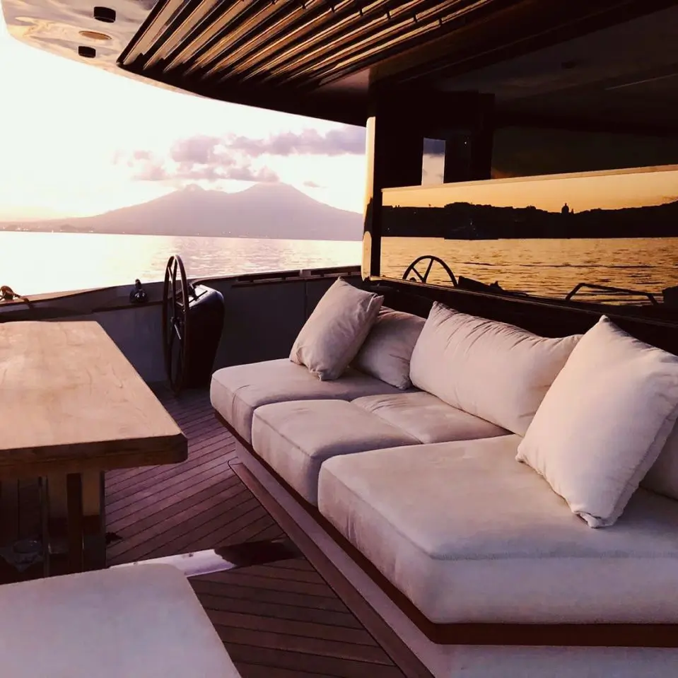 Zona living di uno yacht di lusso con divani chiari, tavolo in legno e ampie vetrate oscurate affacciate sul mare al tramonto, soluzione ideale per privacy, eleganza e comfort visivo in barca.