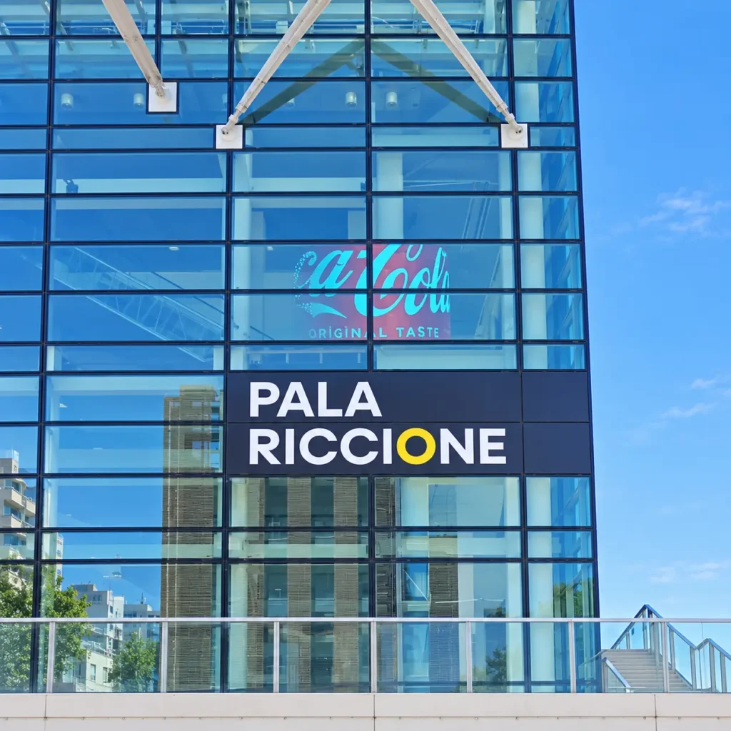 Facciata vetrata del Pala Riccione con contenuto pubblicitario digitale visibile attraverso display LED trasparente integrato nel vetro, soluzione per comunicazione visiva ad alto impatto.