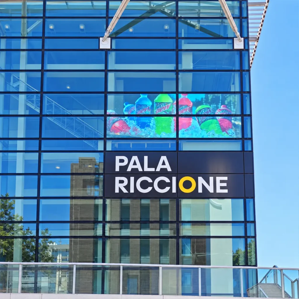 Facciata in vetro del Pala Riccione con display LED trasparente che mostra contenuti pubblicitari digitali, ideale per comunicazione visiva, eventi e installazioni multimediali su superfici vetrate.